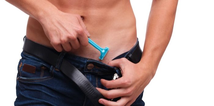 Manscaping - Man wearing a denim pants with black leather belt and holding a blue shaver on right hand.